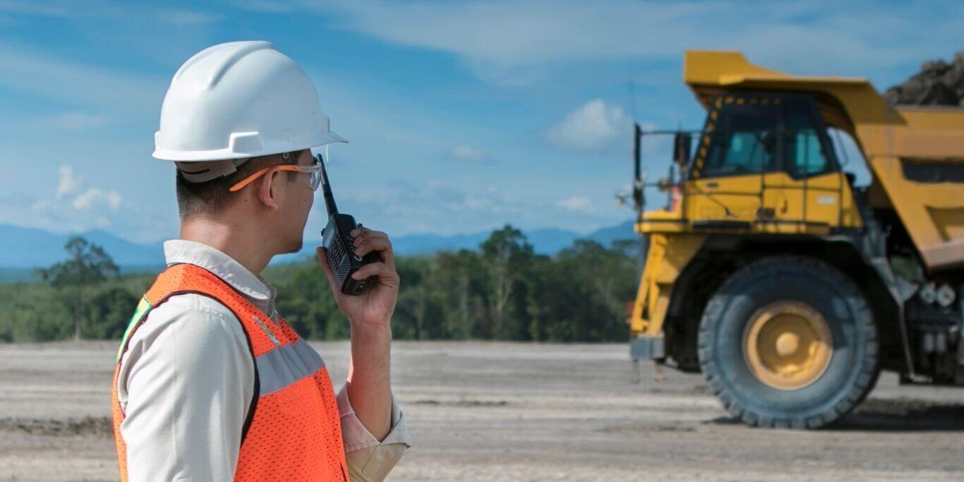 man using a radio to communicate with large truck in background