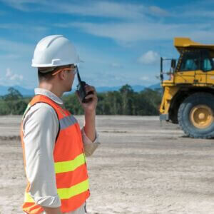 man using a radio to communicate with large truck in background